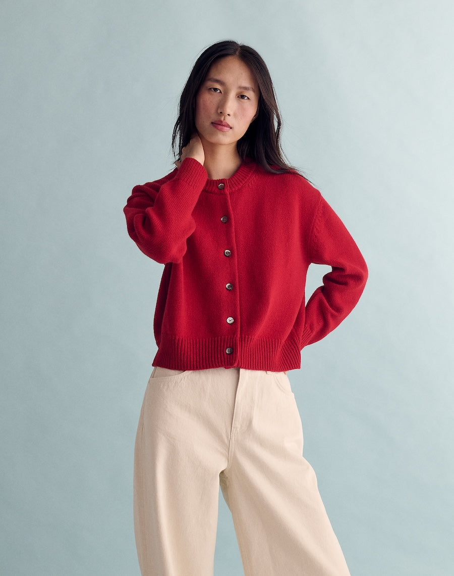 Person wearing a red cardigan and beige pants against a light gray background