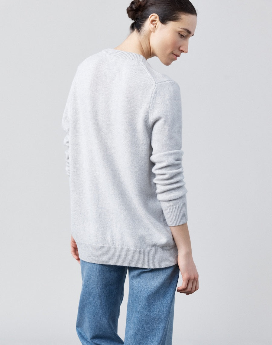 Person wearing a light gray sweater and blue jeans on a plain background