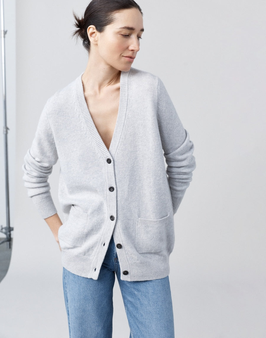 Woman wearing a light gray cardigan over a white shirt with blue jeans on a plain background