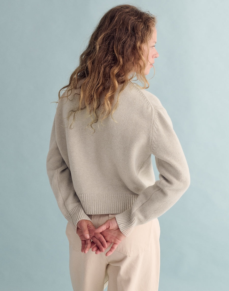 Woman wearing a beige sweater and pants against a light blue background