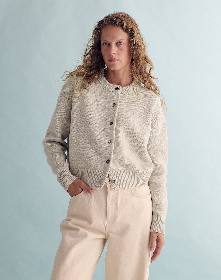 Woman wearing a beige cardigan and pants against a light blue background