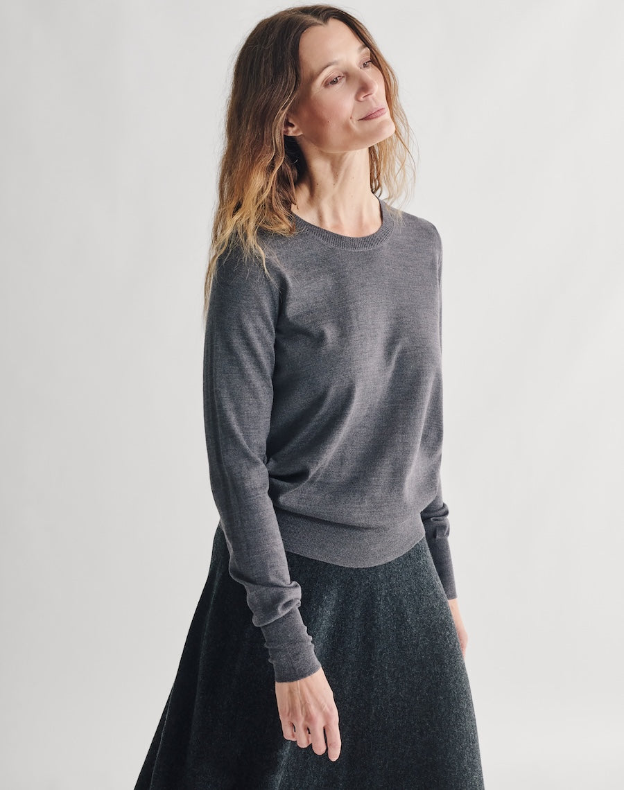 Woman wearing a gray sweater and dark skirt on a white background