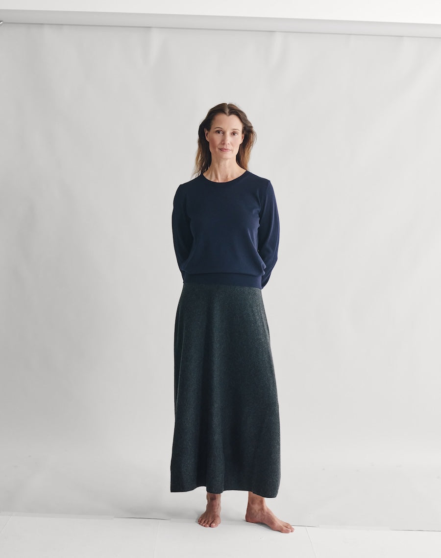 Woman wearing a navy sweater and dark green skirt against a white background