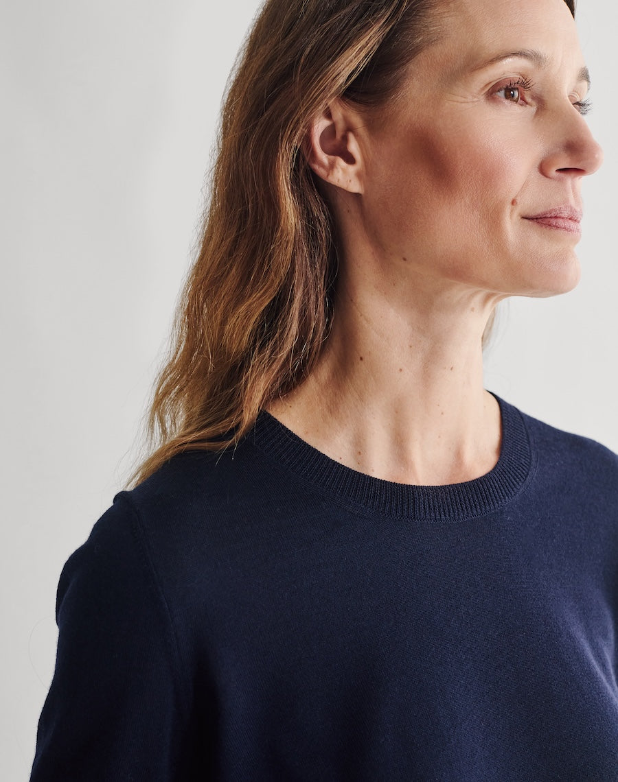 Woman wearing a navy sweater and dark skirt against a plain background