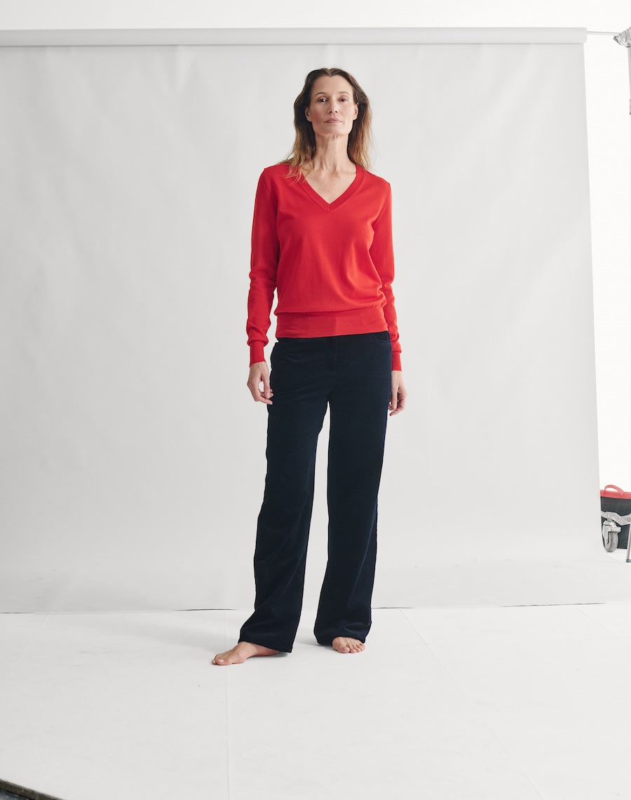 Woman wearing a red sweater and black pants standing against a white background
