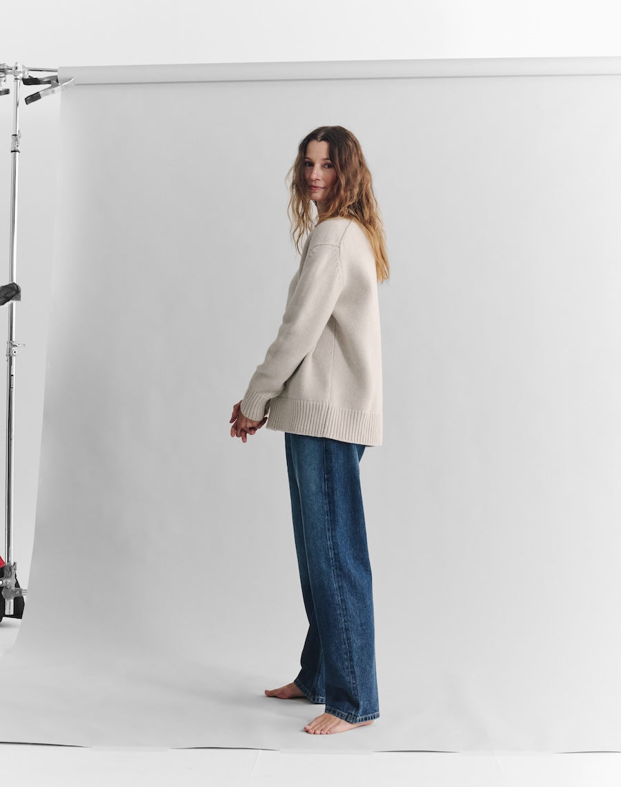 Woman wearing a white sweater and blue jeans standing against a white background