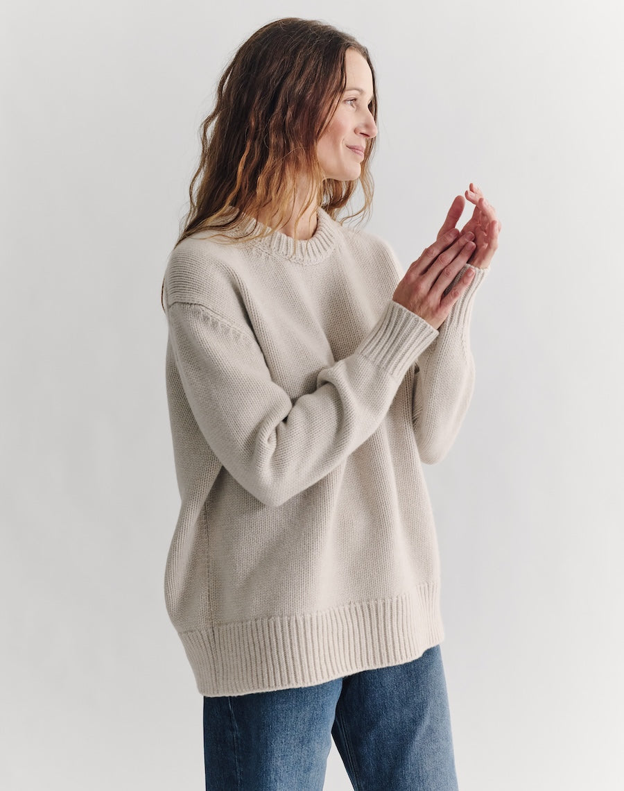 Woman wearing a beige sweater and blue jeans on a white background
