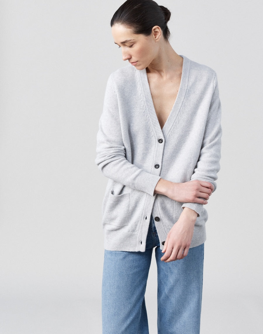 Woman wearing a light gray cardigan over a white shirt with blue jeans on a plain background