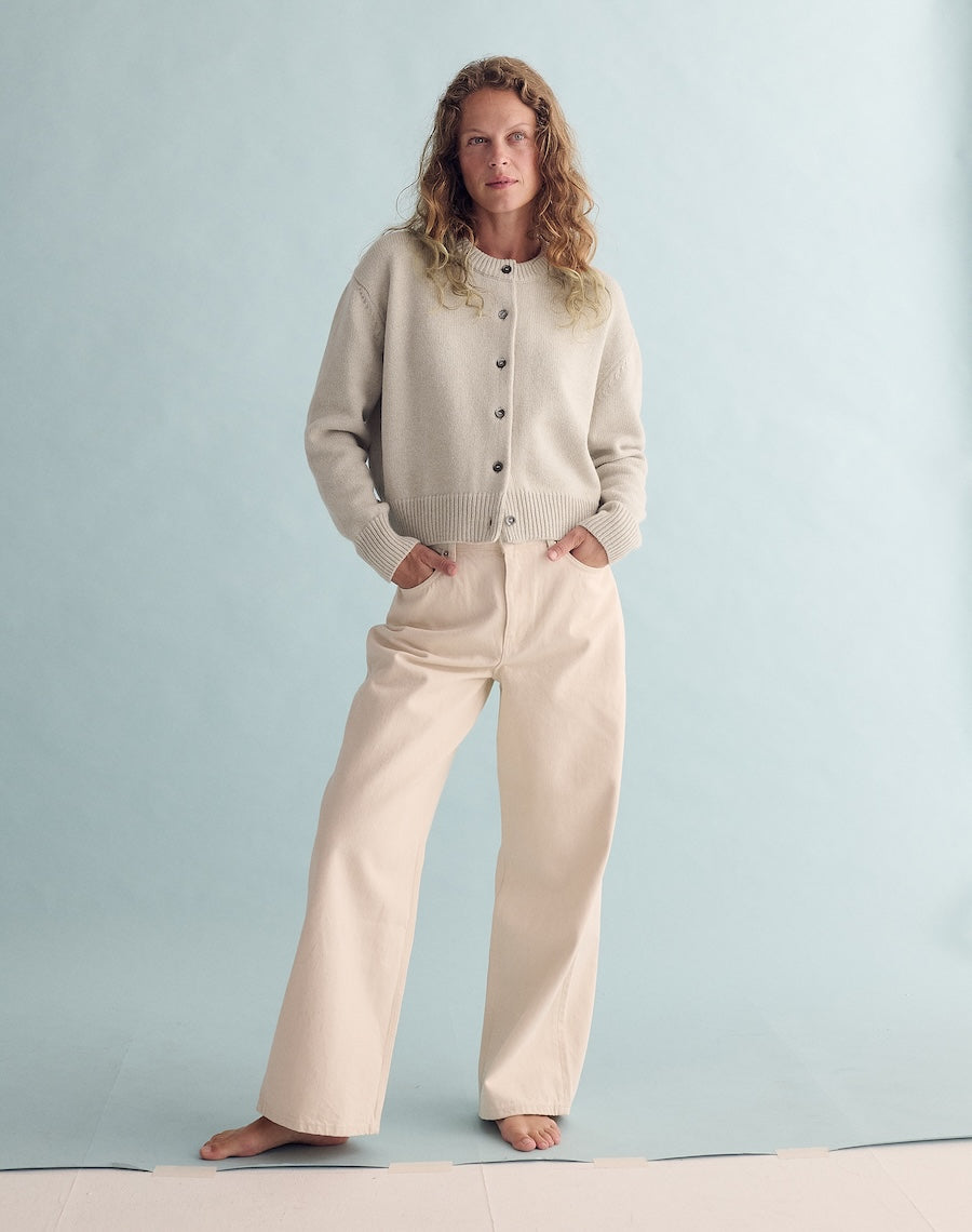 Woman wearing a beige cardigan and pants against a light blue background