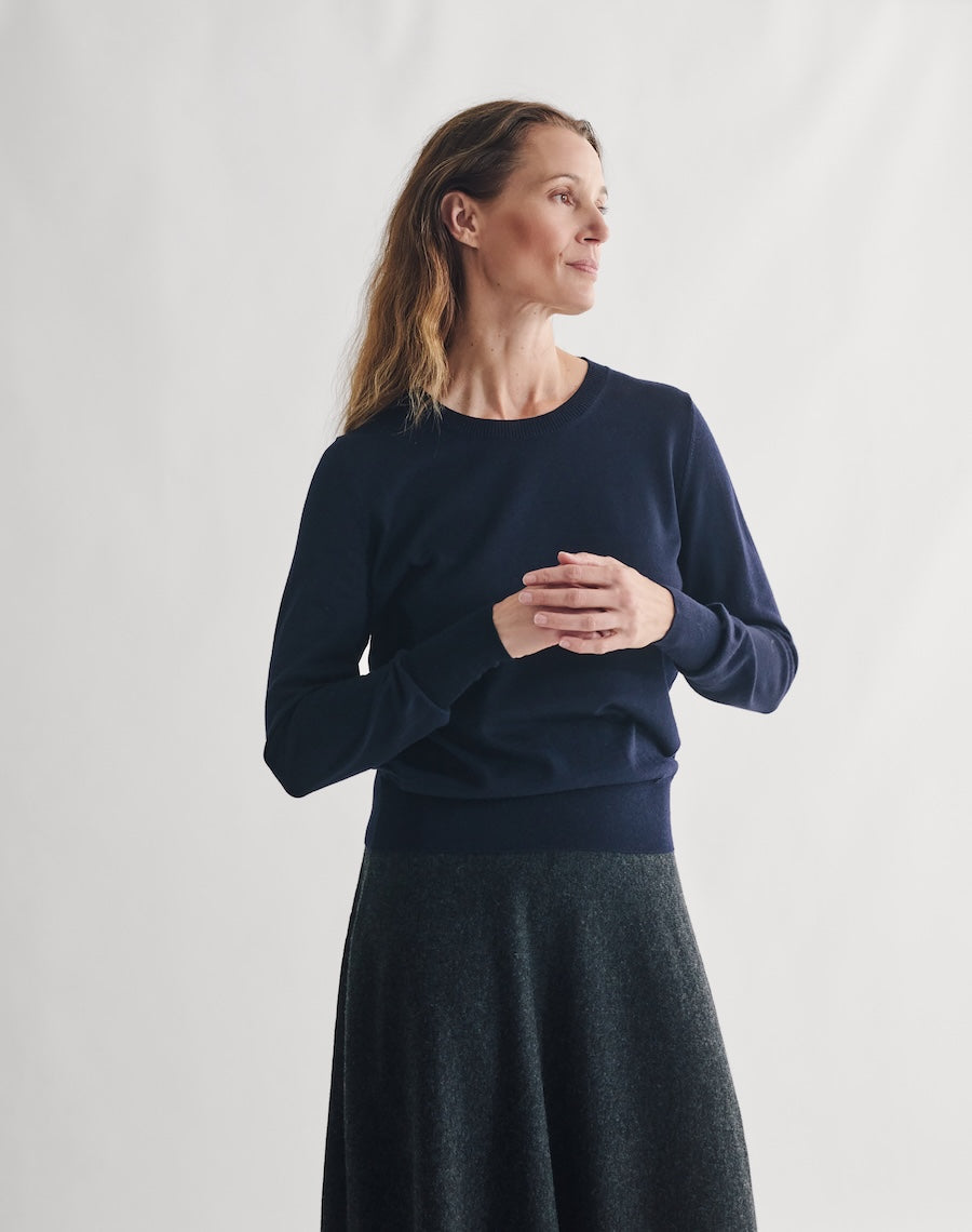 Woman wearing a navy sweater and dark skirt against a plain background