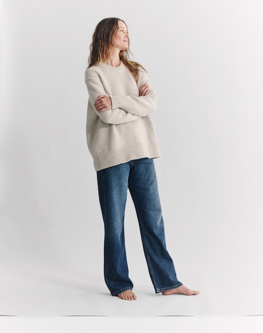 Woman wearing a beige sweater and blue jeans on a white background