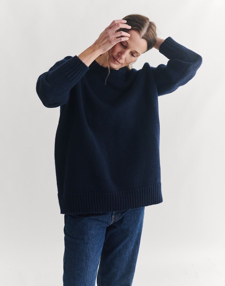 Person wearing a navy sweater and blue jeans against a white background