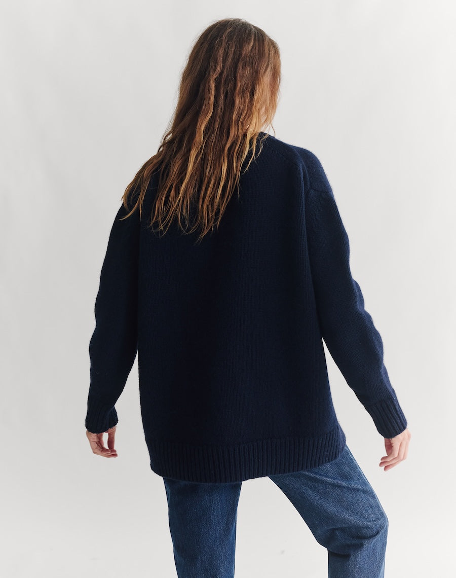 Person wearing a navy sweater and blue jeans against a white background